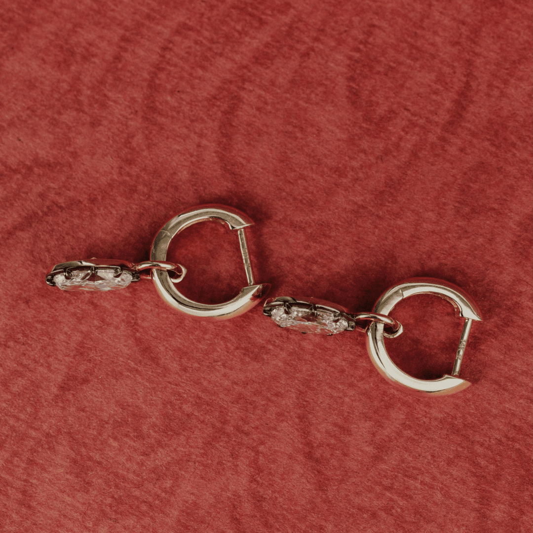 14k gold round cut, lab grown diamond dangle earrings with Black Rhodium featured on a textured red surface. 