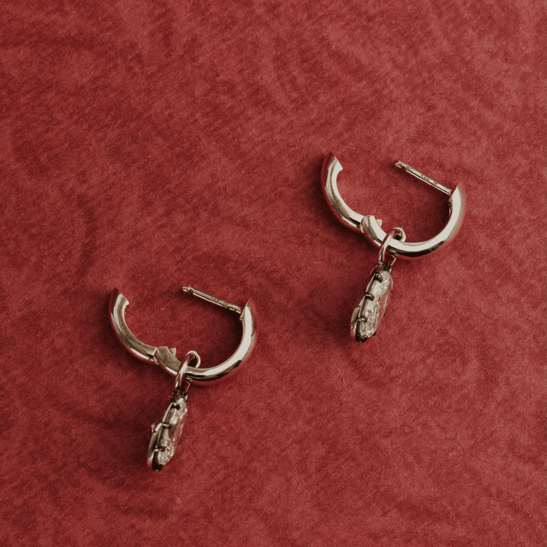 14k gold round cut, lab grown diamond dangle earrings with Black Rhodium featured on a textured red surface. 