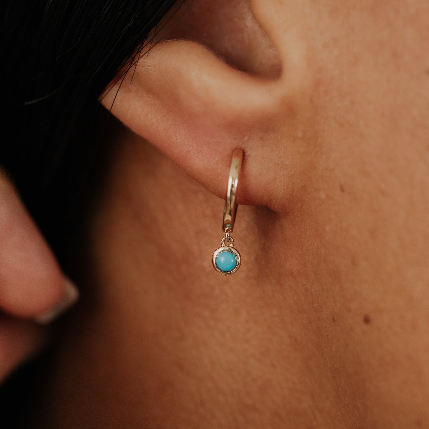 Close-up of an ear wearing a gold hoop earring with a turquoise stone.