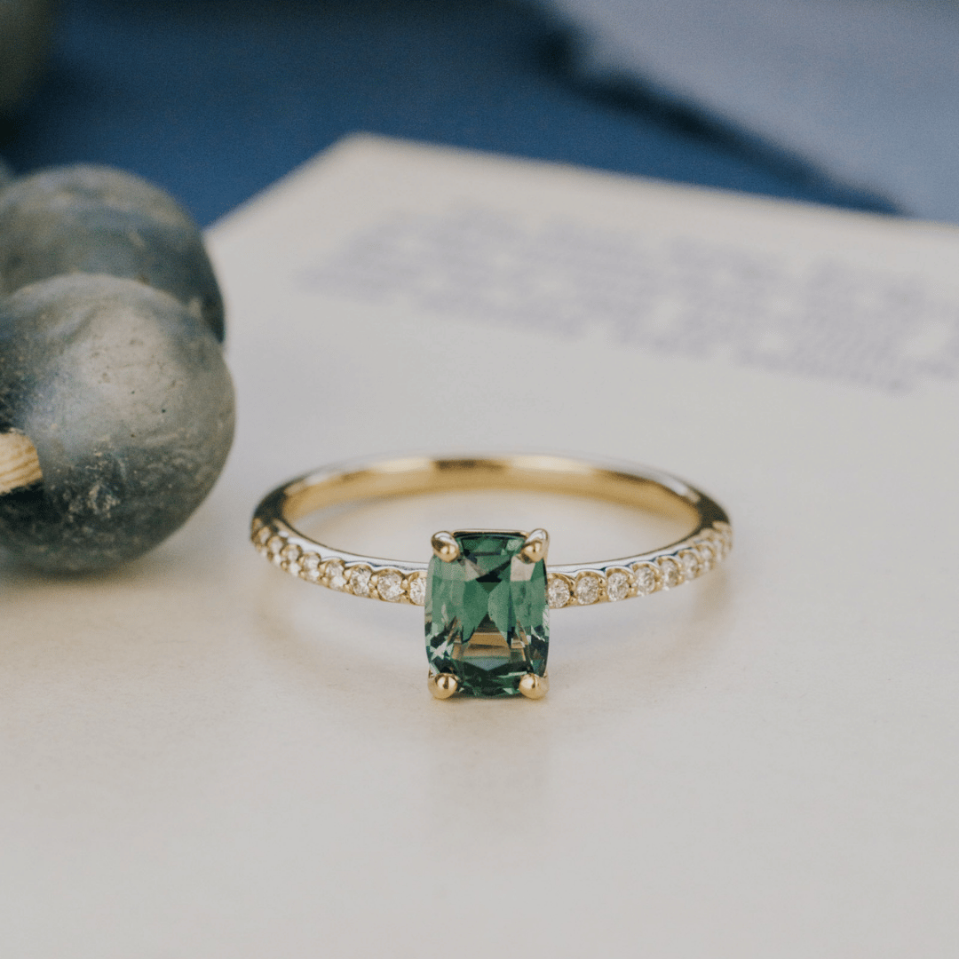 A 14k gold ring featuring a single blue sapphire gemstone, displayed on a white surface with a soft-focus background.