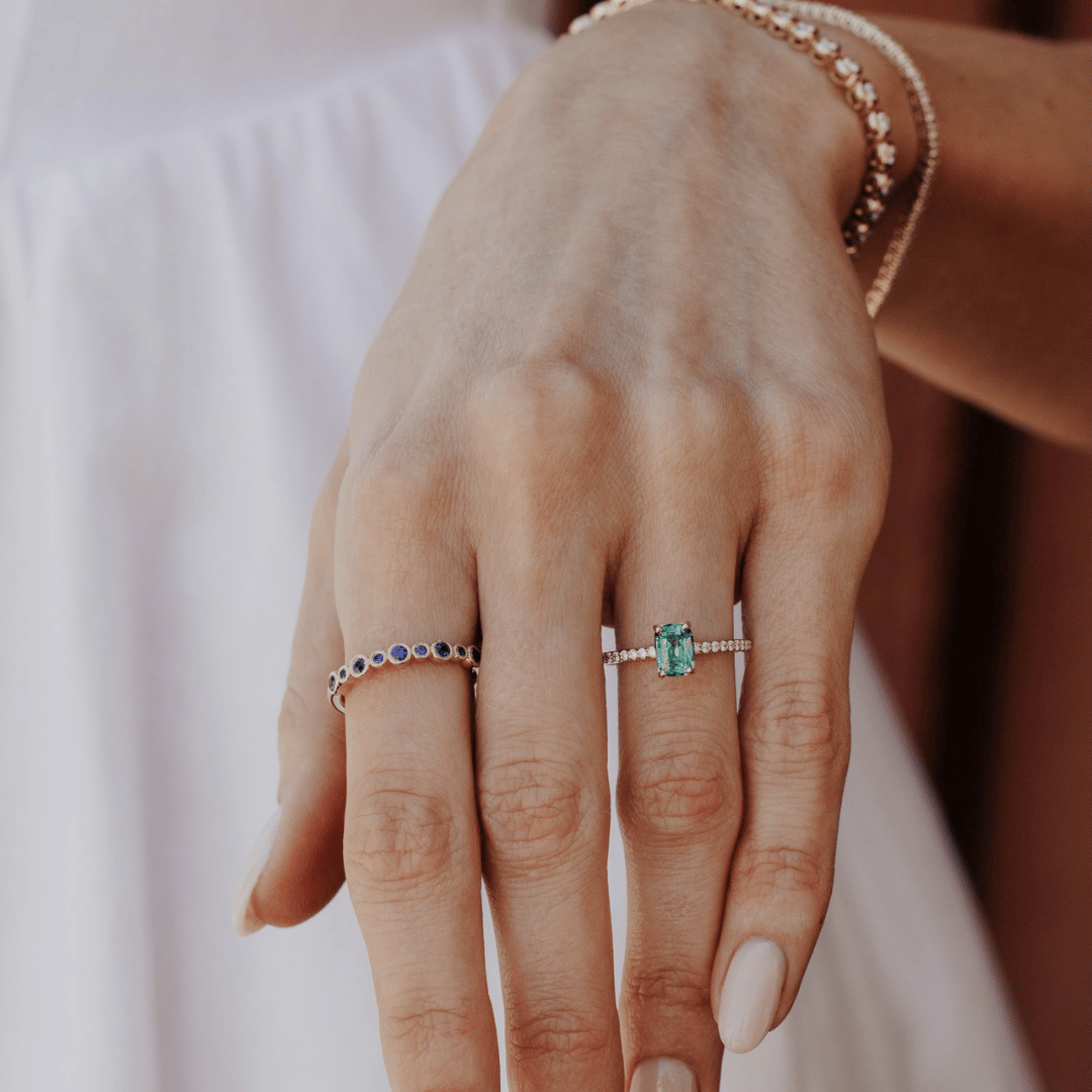 A 14k gold ring featuring a single blue sapphire gemstone, displayed on the ring finger of a hand model