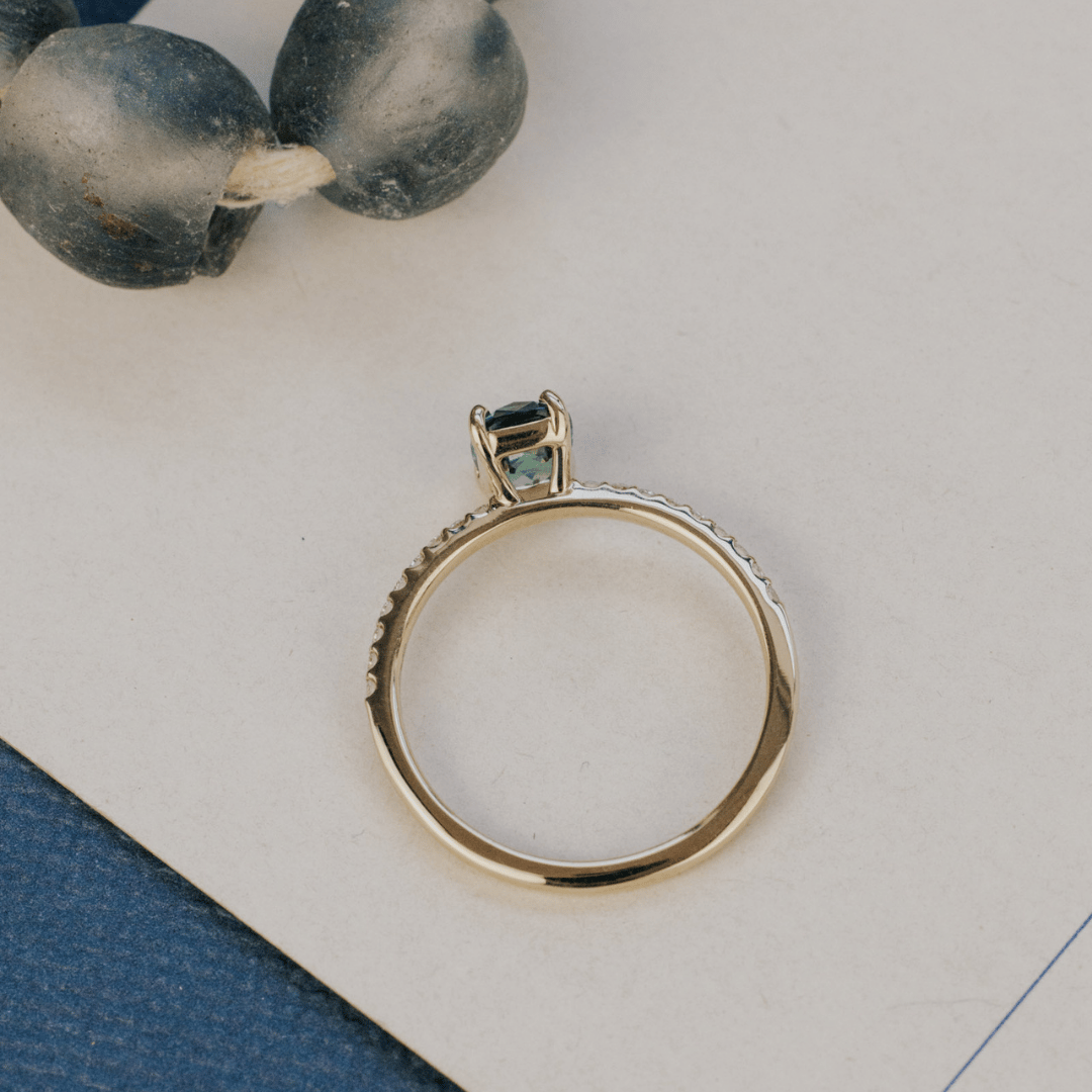A 14k gold ring featuring a single blue sapphire gemstone from a top view, displayed on a white surface with a soft-focus background.
