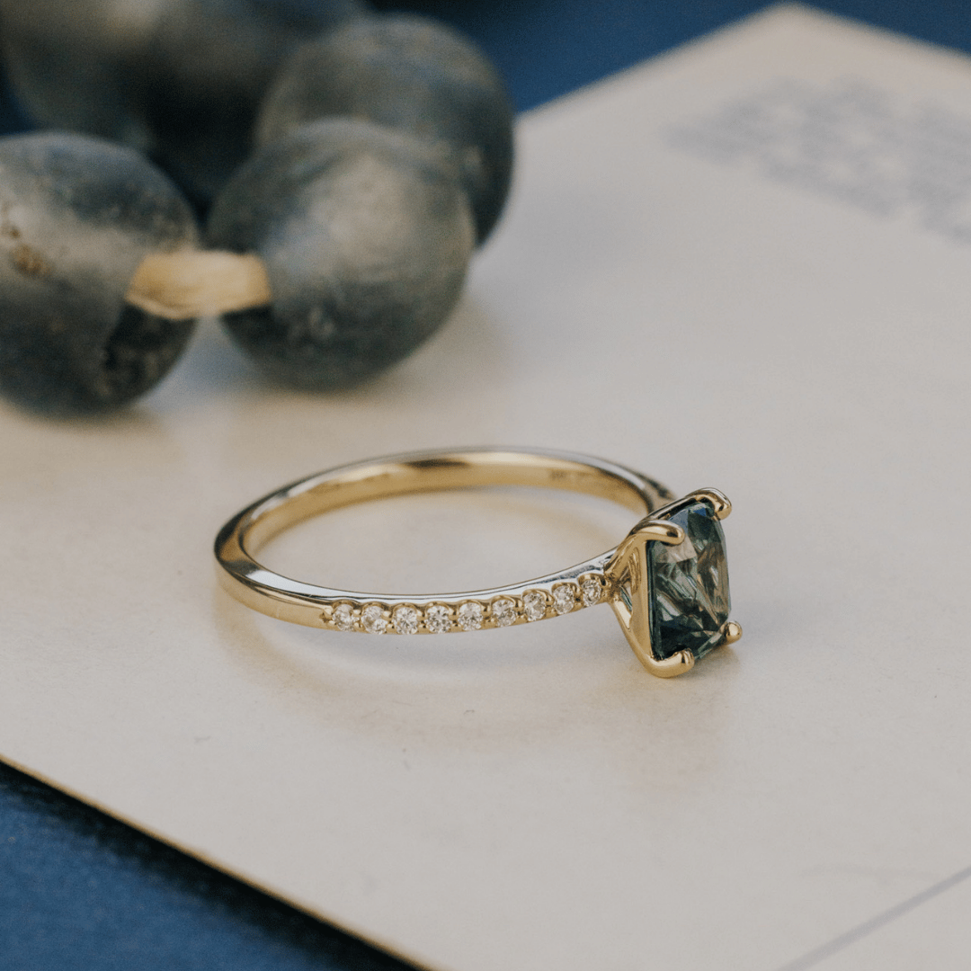 A 14k gold ring featuring a single blue sapphire gemstone, displayed on a white surface with a soft-focus background.