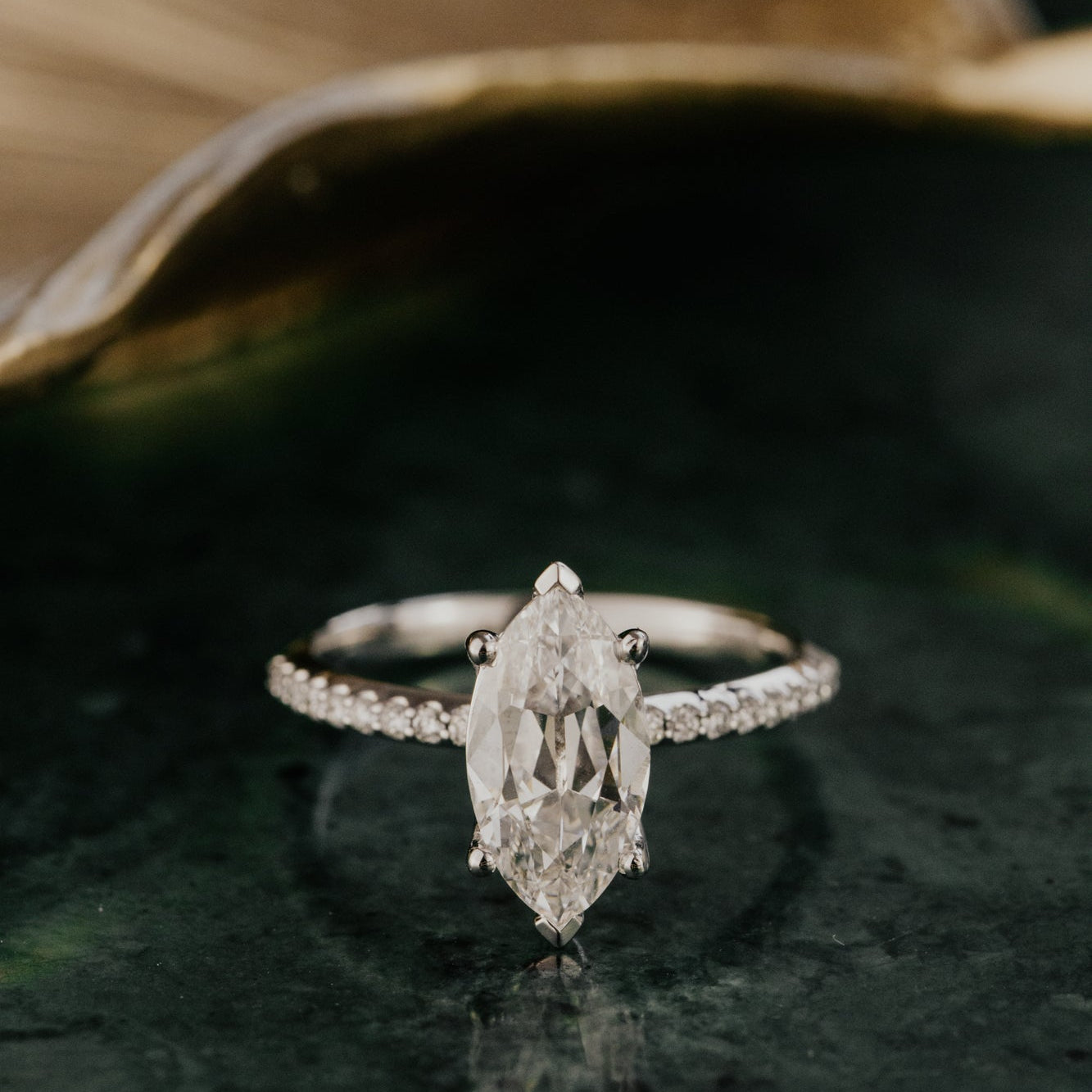Old mine cut marquise lab grown diamond ring on a dark green surface.
