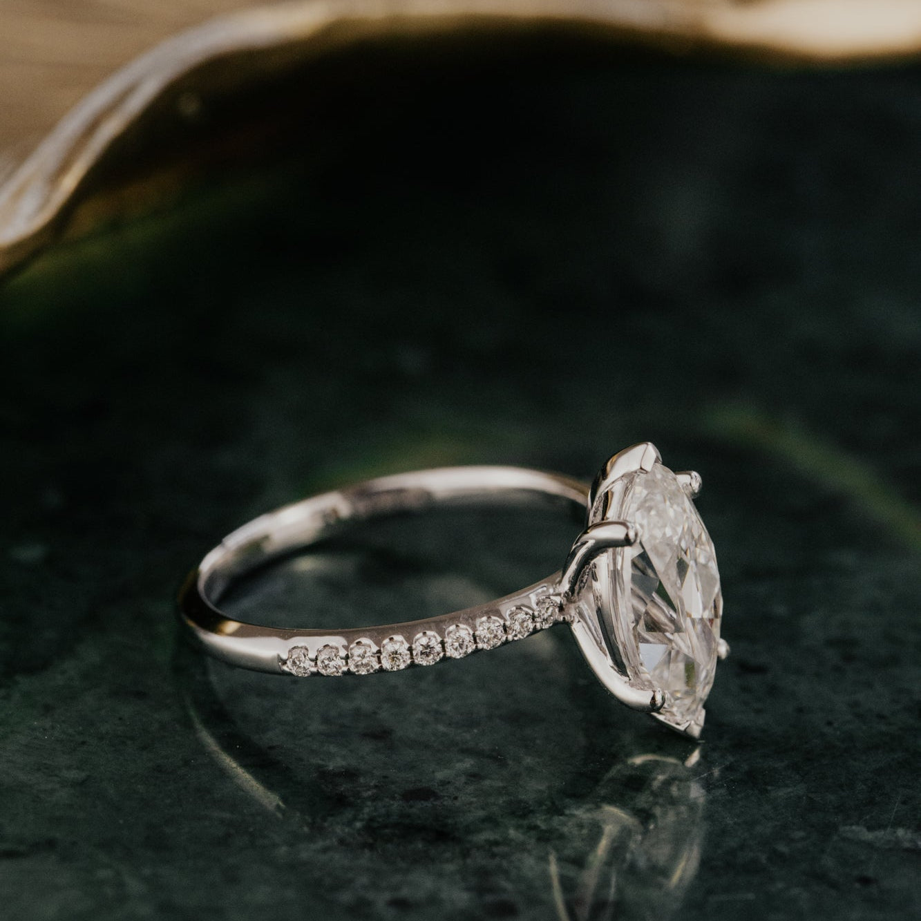 Marquise diamond ring with a pave diamond band on a dark green surface with a blurred background.
