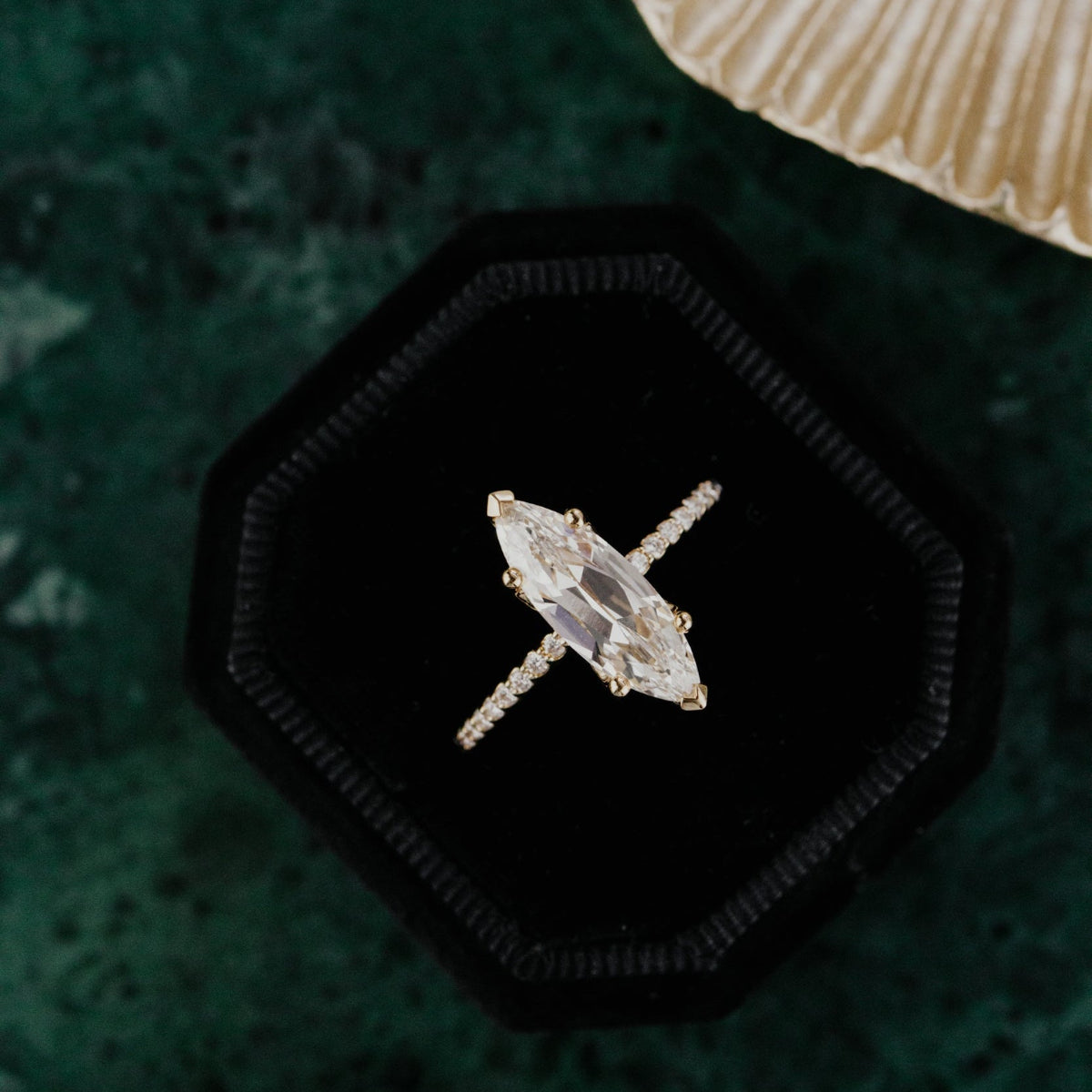 Lab grown diamond ring in a black hexagonal box on a textured green surface with a beige shell.