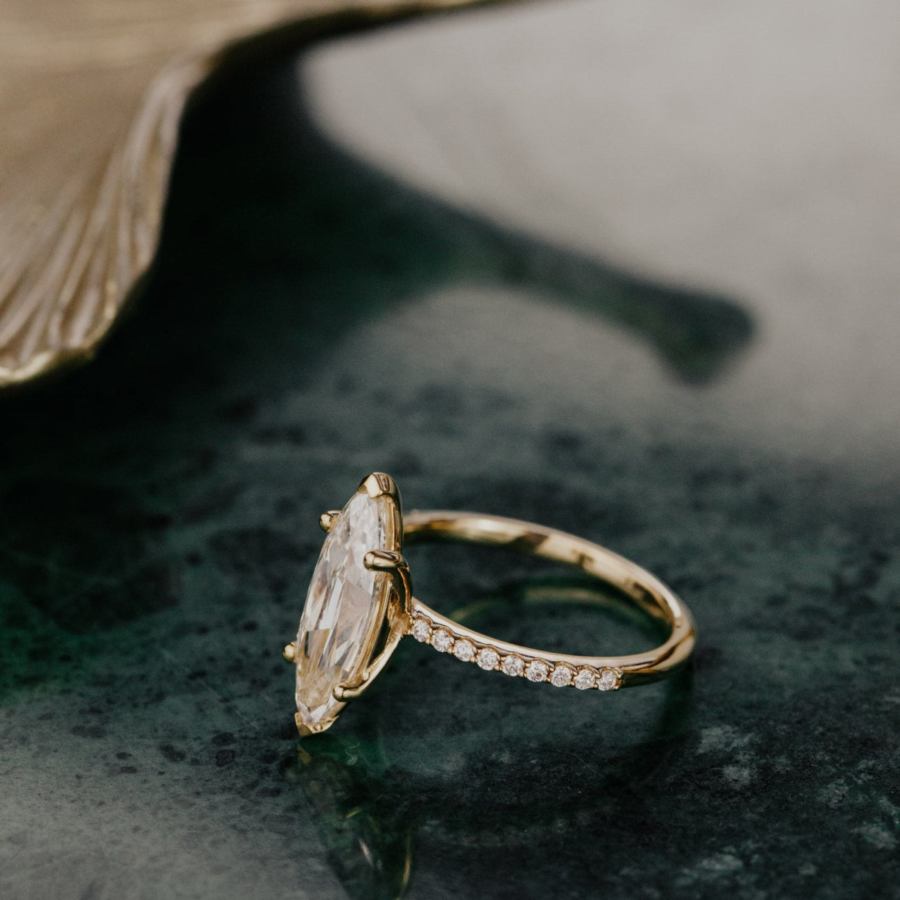 Gold ring with a large lab grown diamond and smaller diamonds on a dark surface.