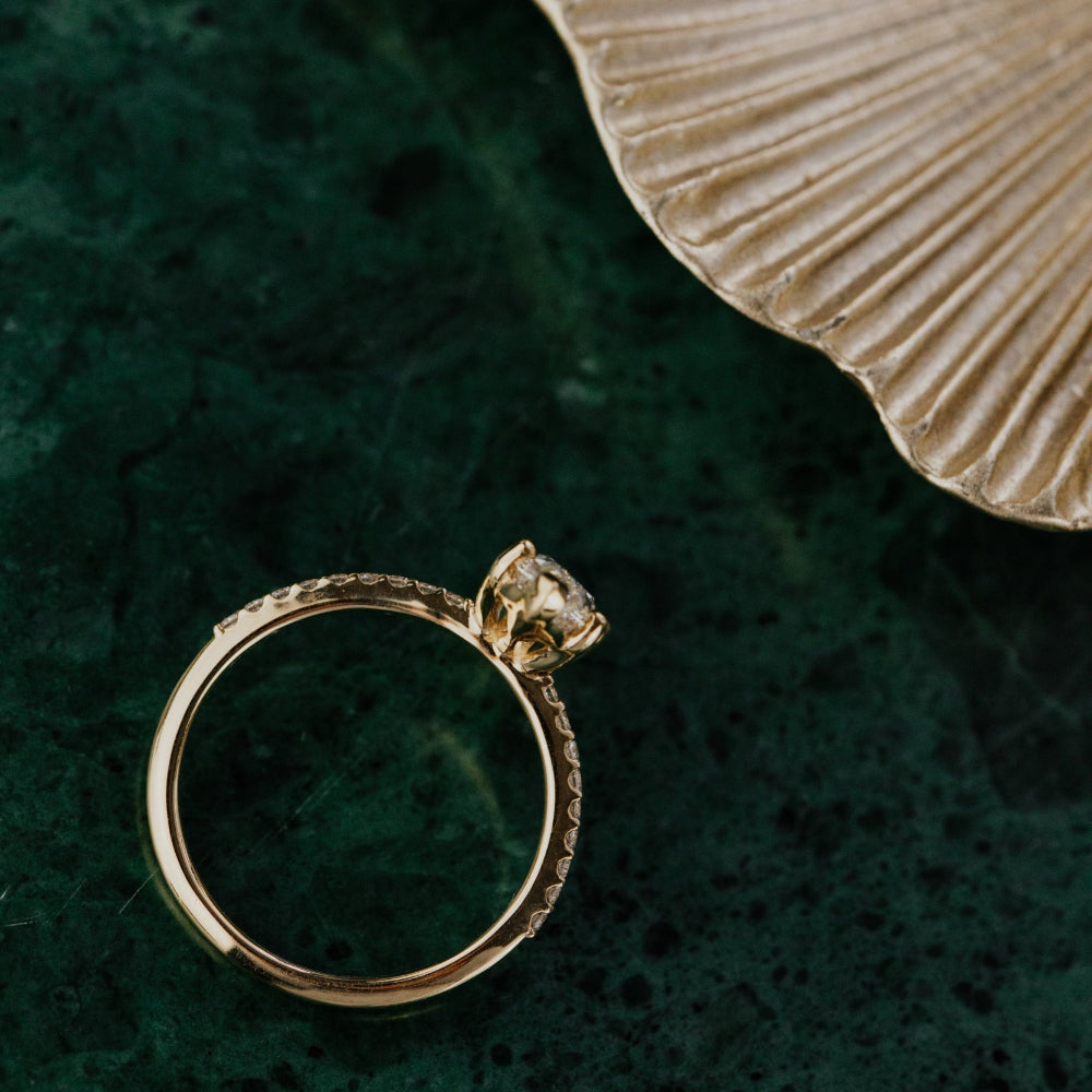 Gold ring with a lab grown diamond on a green surface with a beige leaf.