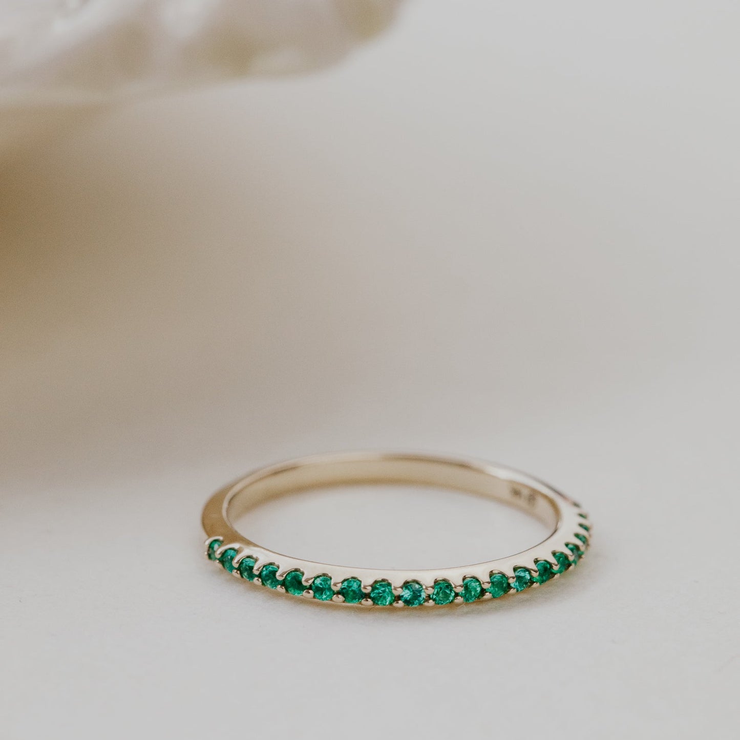 Gold wedding band with green emerald gemstones on a soft white background.