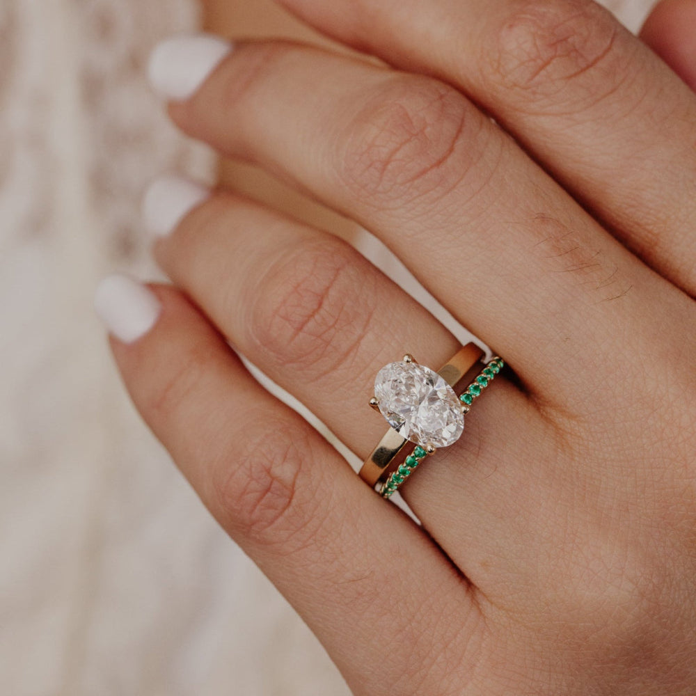Close-up of a hand wearing a diamond ring with emerald wedding band.