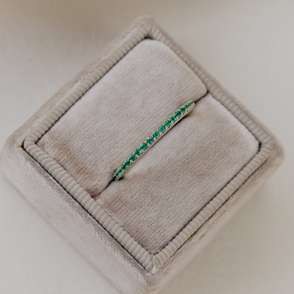 Green emerald wedding band on a beige velvet jewelry box.