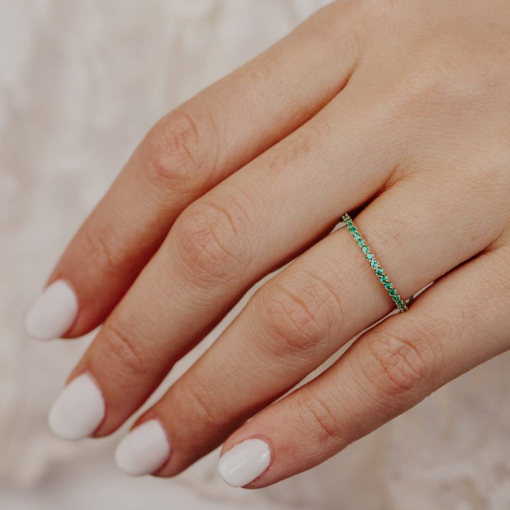 Close-up of a hand wearing a green emerald wedding band with a blurred background.