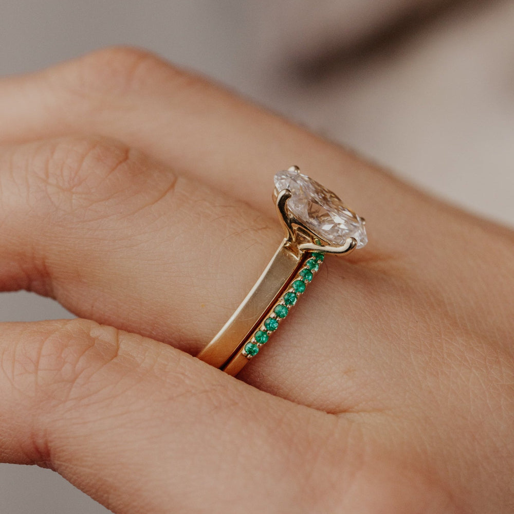 Close-up of a hand wearing two rings with a large diamond and green emerald wedding band.