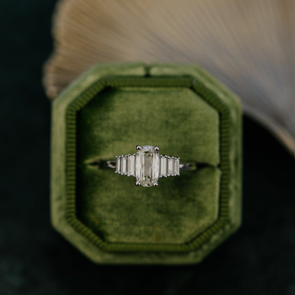 Elongated Cushion Diamond ring in a green velvet box with a blurred background.