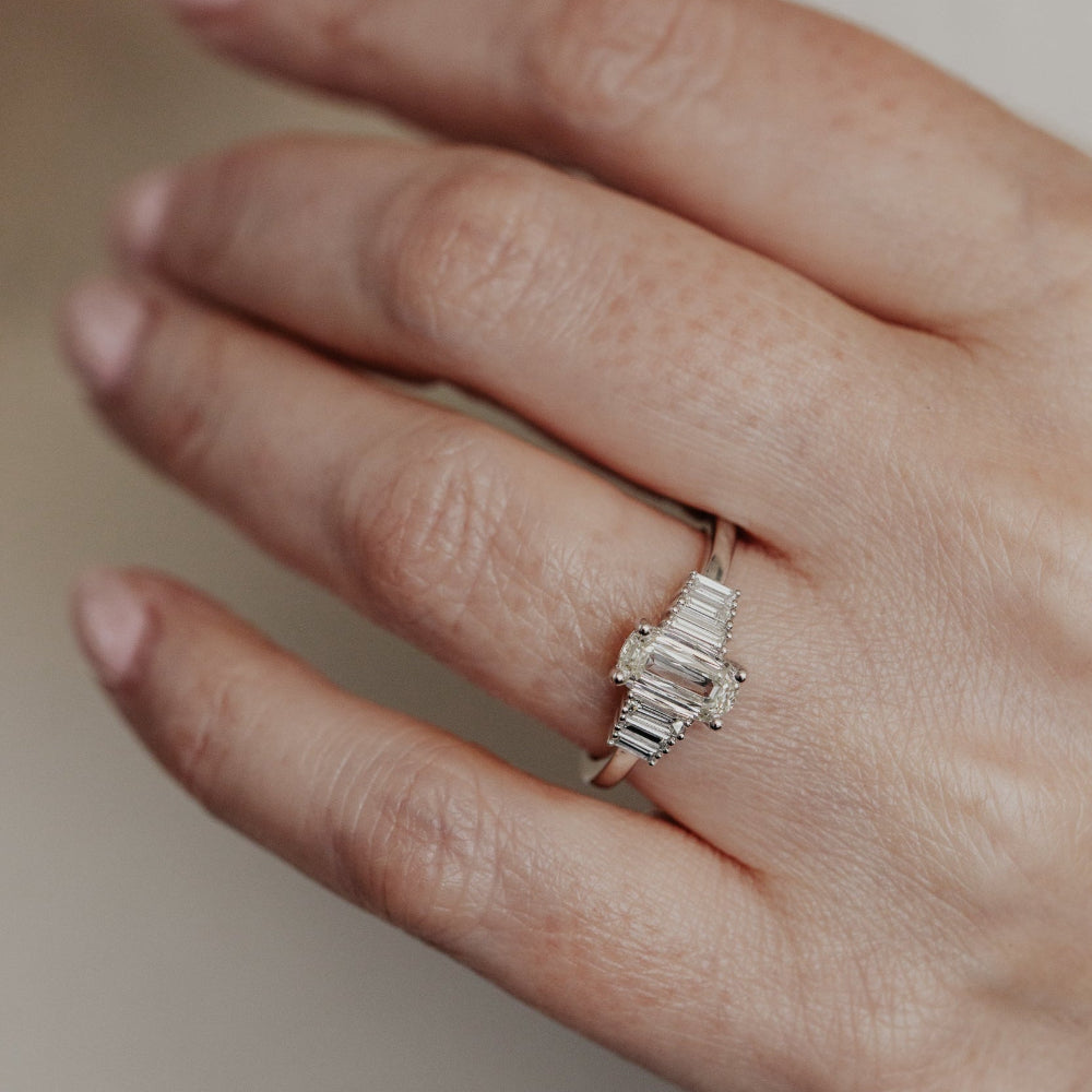 White gold ring with a elongated cushion diamonds on a person's finger against a neutral background.