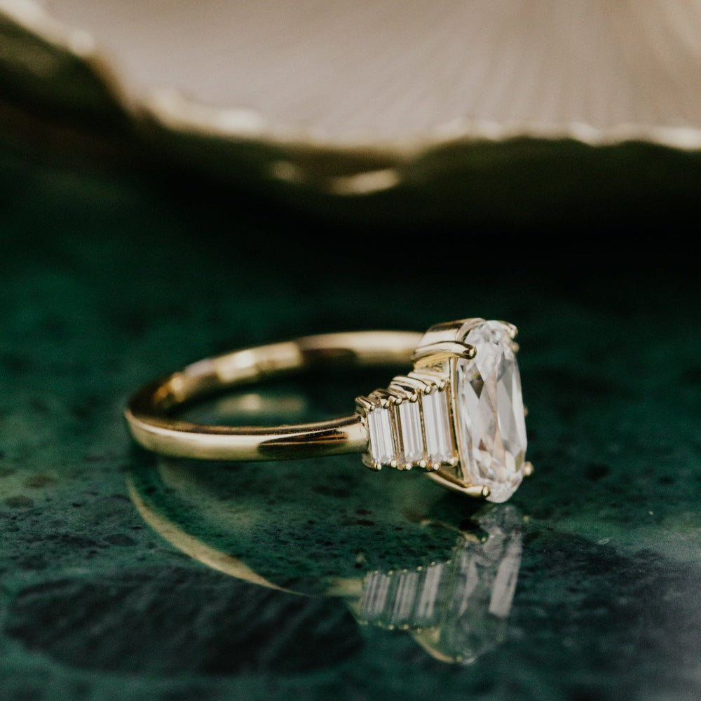 Gold ring with a elongated cushion diamond on a green surface.