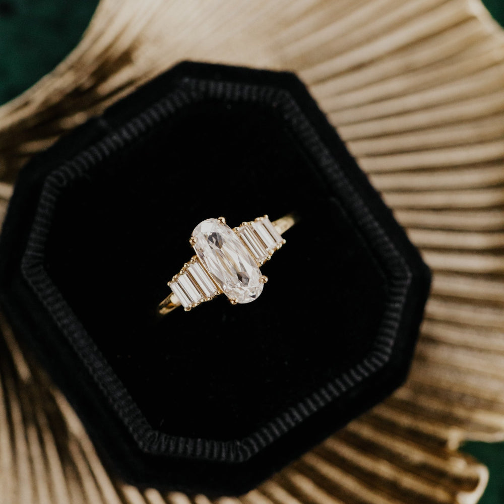 Gold engagement ring with a large elongated cushion diamond on a black hexagonal box.