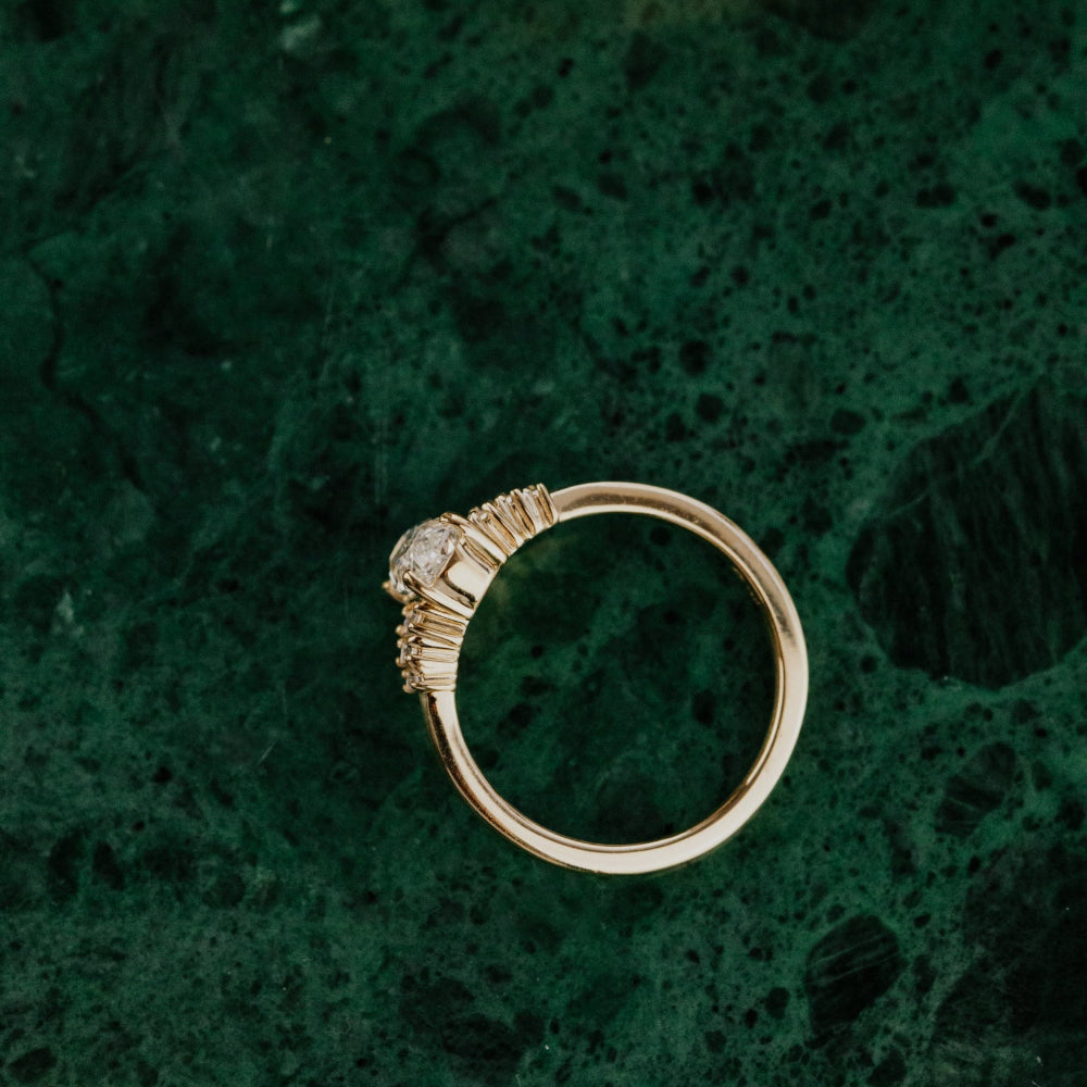 Gold engagement ring with a elongated cushion diamond on a textured green surface.