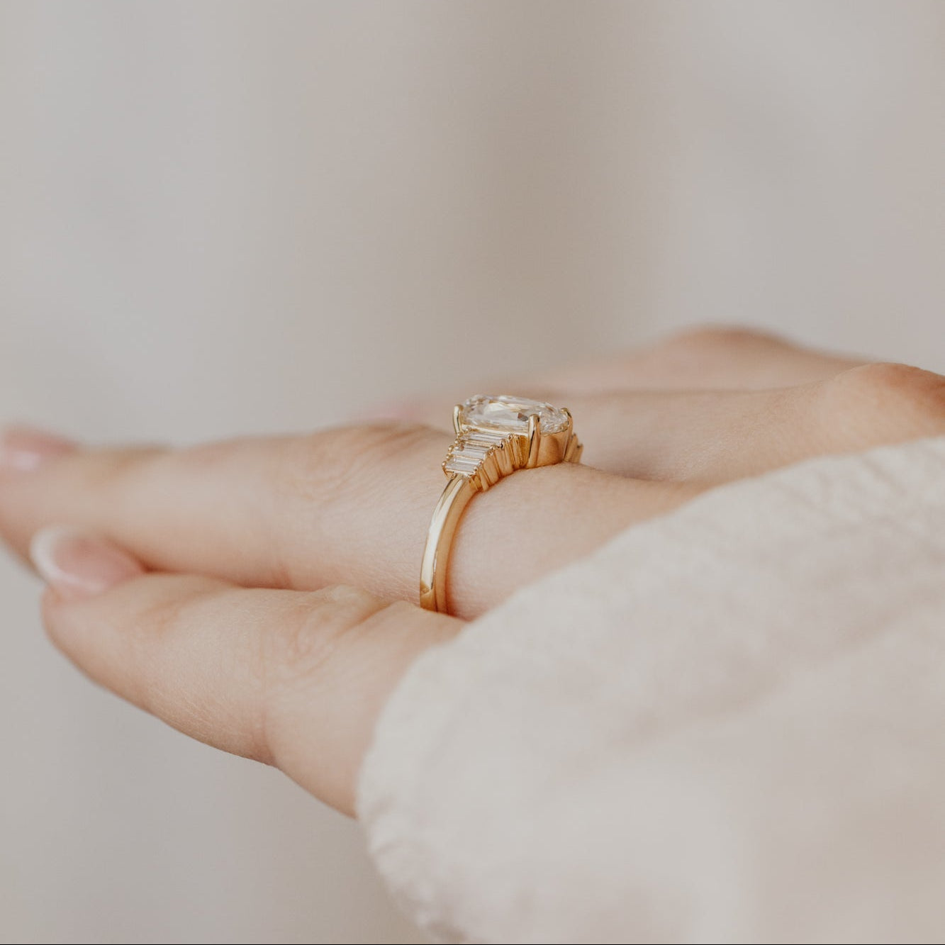 Gold ring with a elongated cushion diamond on a person's finger against a neutral background.