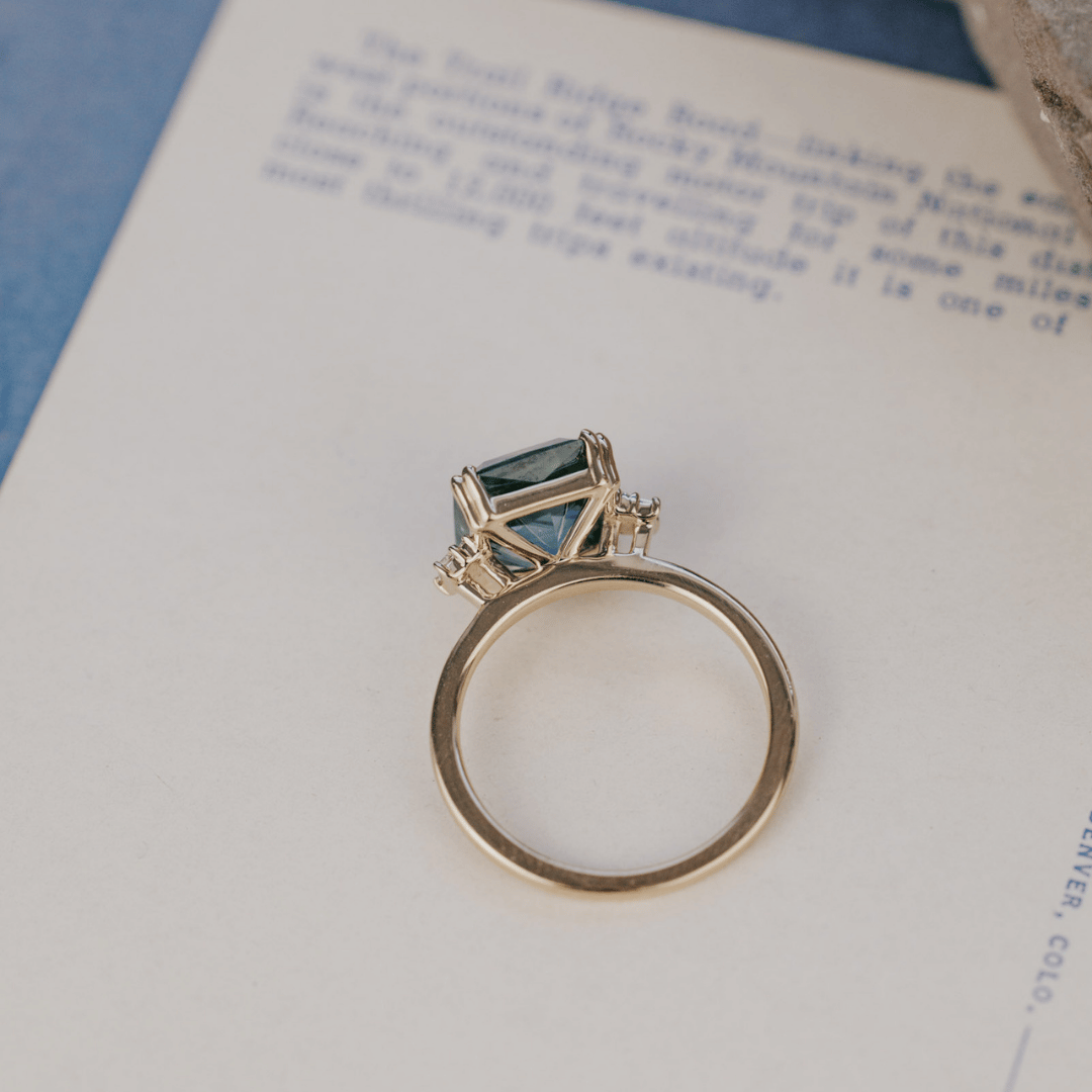 A 14k gold ring featuring a blue sapphire gemstone viewed from above displayed on a textured white surface with a soft-focus background.