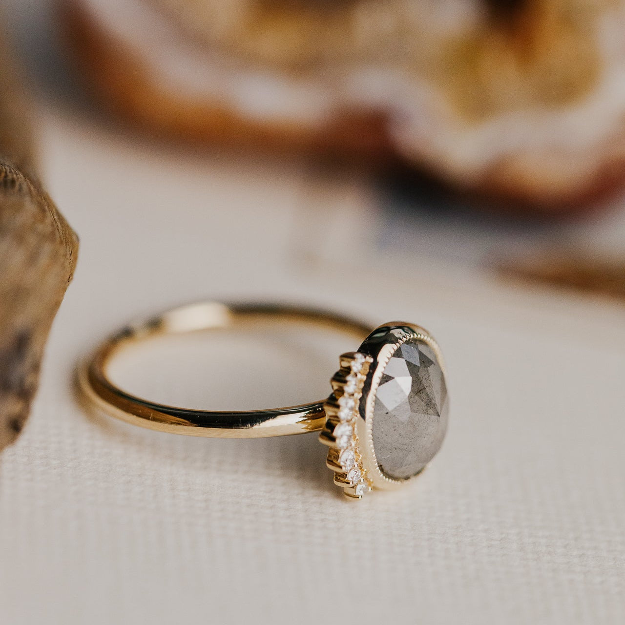 Gold ring with a gray oval rustic diamond on a neutral background.