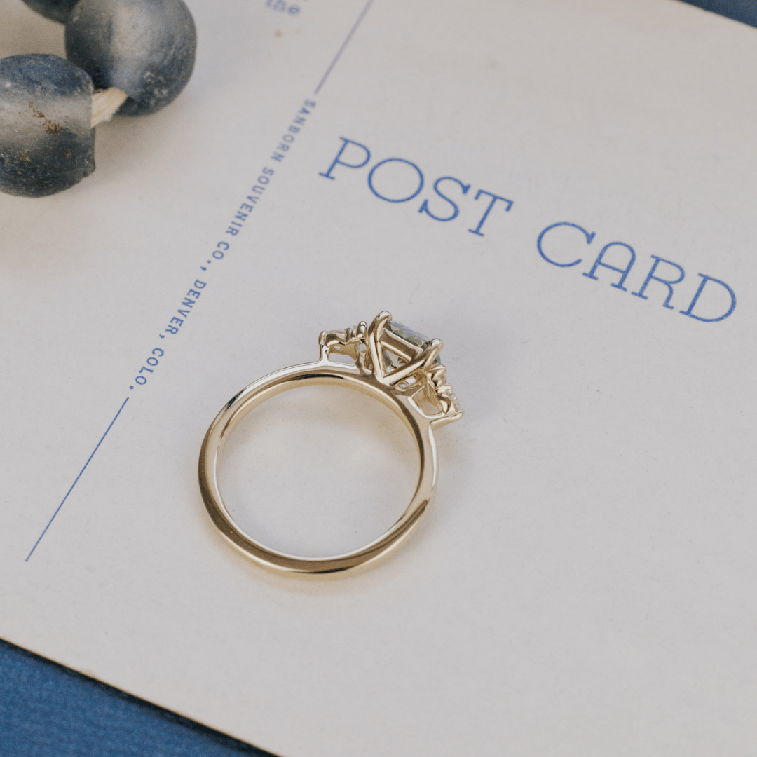 A 14k gold ring featuring a yellow-green sapphire gemstone, from the top view, displayed on a white surface with a soft background. 