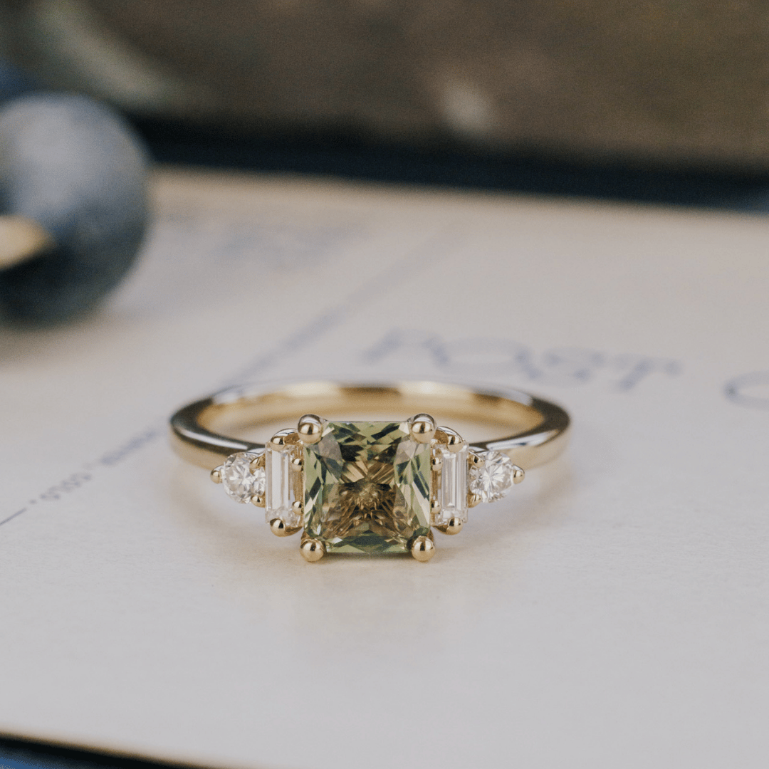 A 14k gold ring featuring a yellow-green sapphire gemstone, displayed on a white surface with a soft background. 