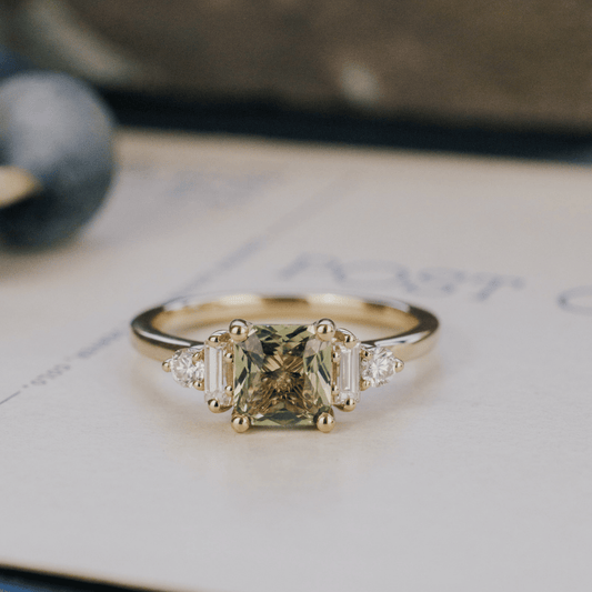 A 14k gold ring featuring a yellow-green sapphire gemstone, displayed on a white surface with a soft background. 