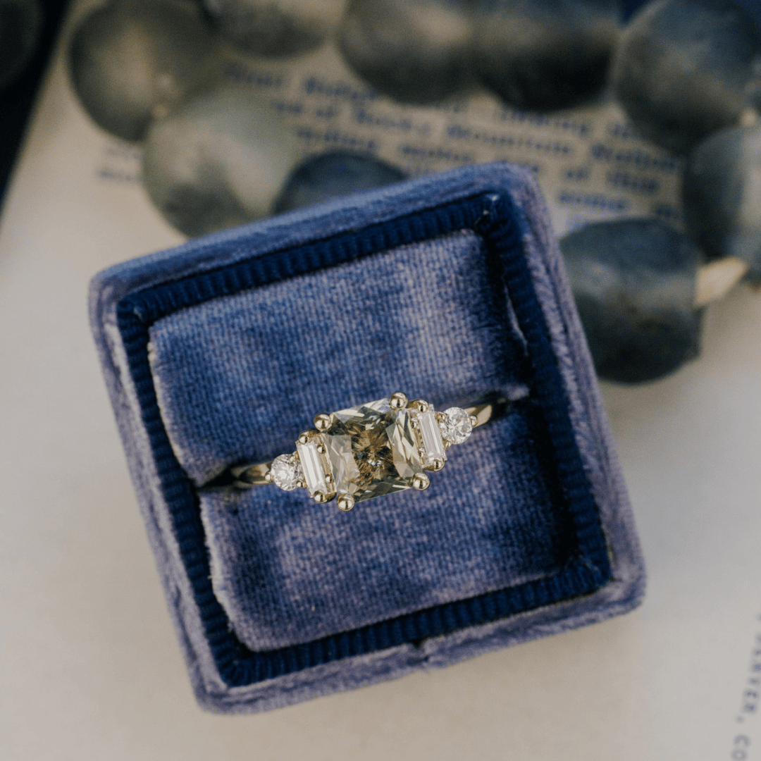 A 14k gold ring featuring a yellow-green sapphire gemstone, displayed in a ring box with a soft-focus background.