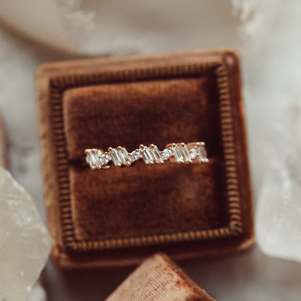 Diamond wedding band in a brown velvet box with crystals in the background.