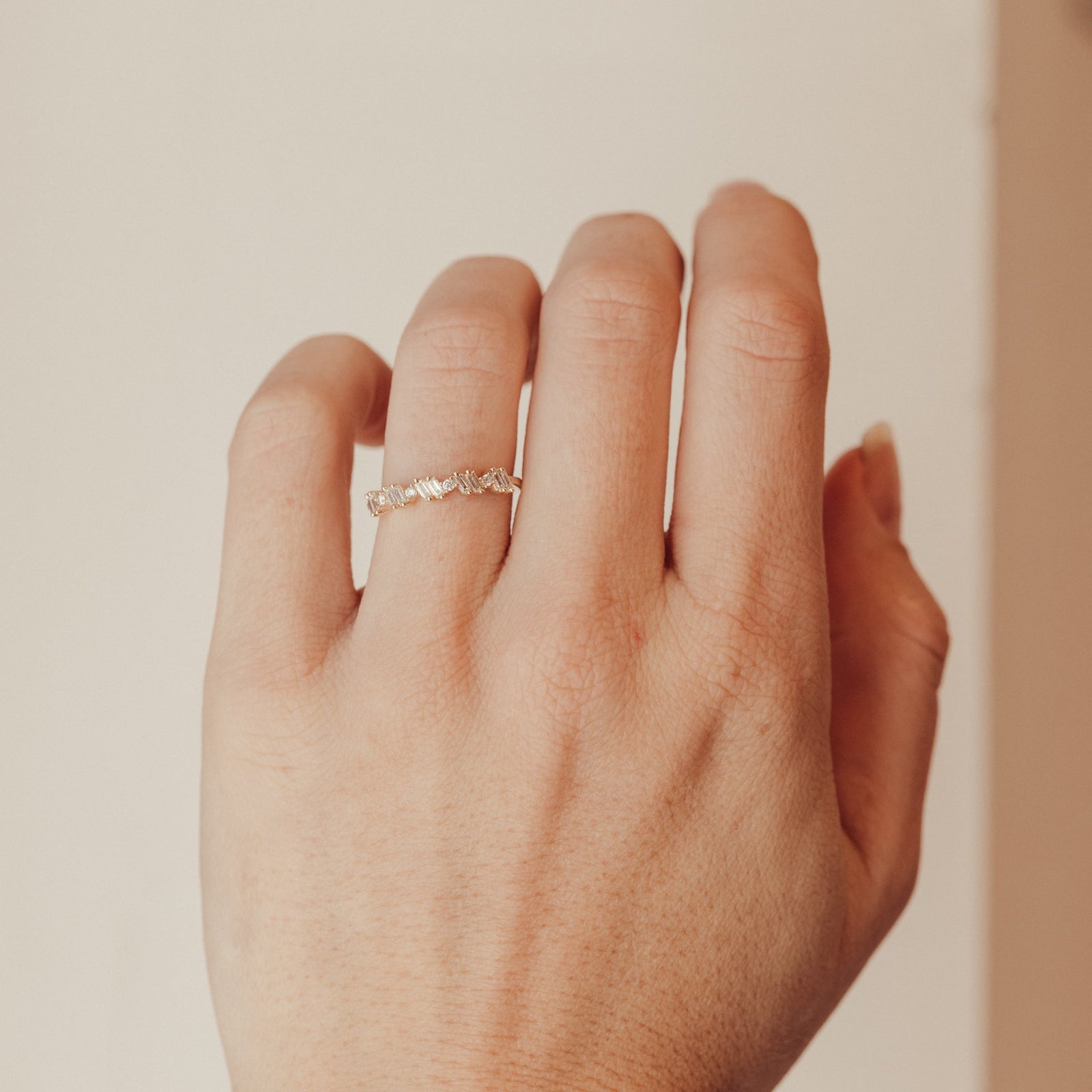 Hand with a diamond wedding band on a plain background.