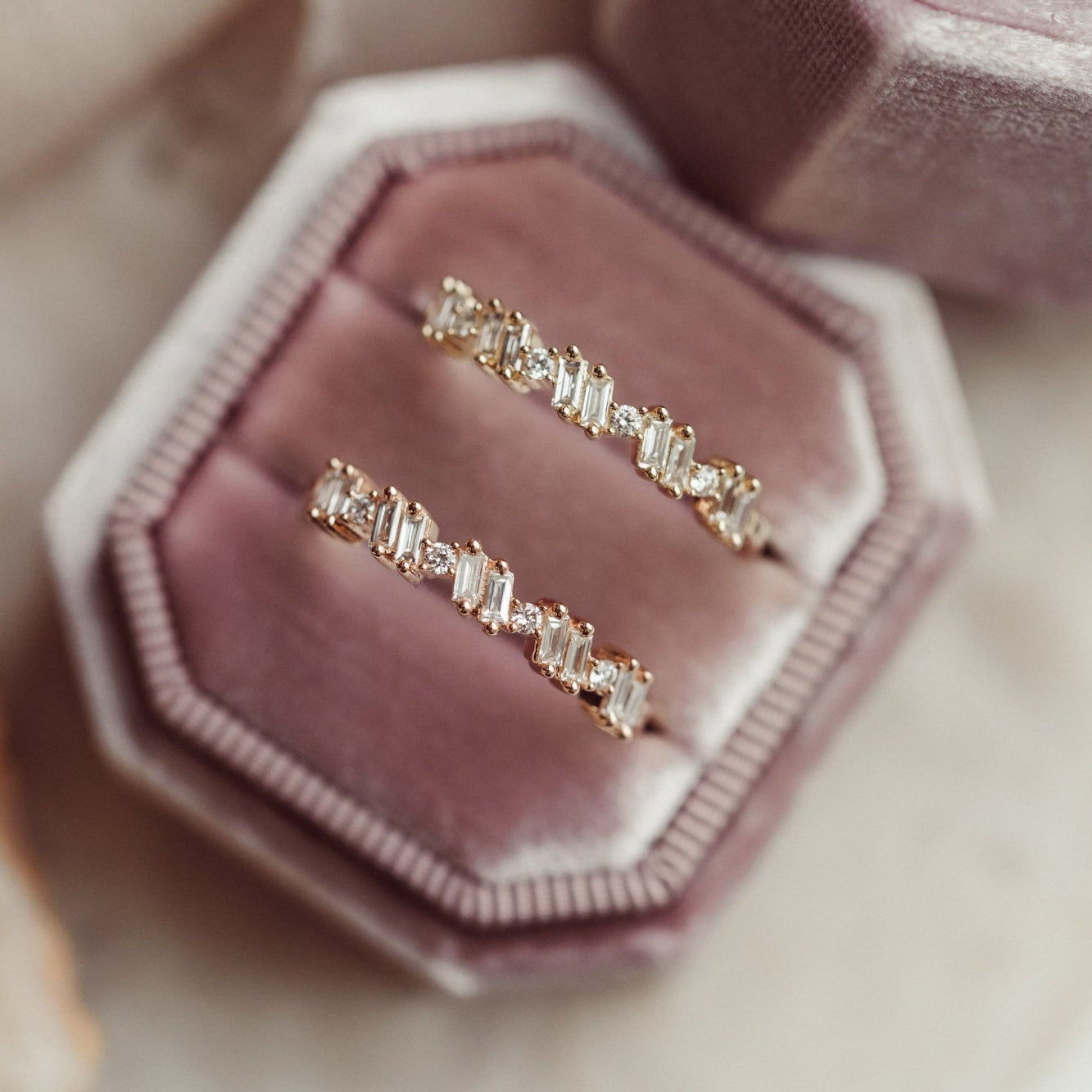 Two diamond wedding band in 14k yellow and rose gold in a pink velvet box on a soft beige background.
