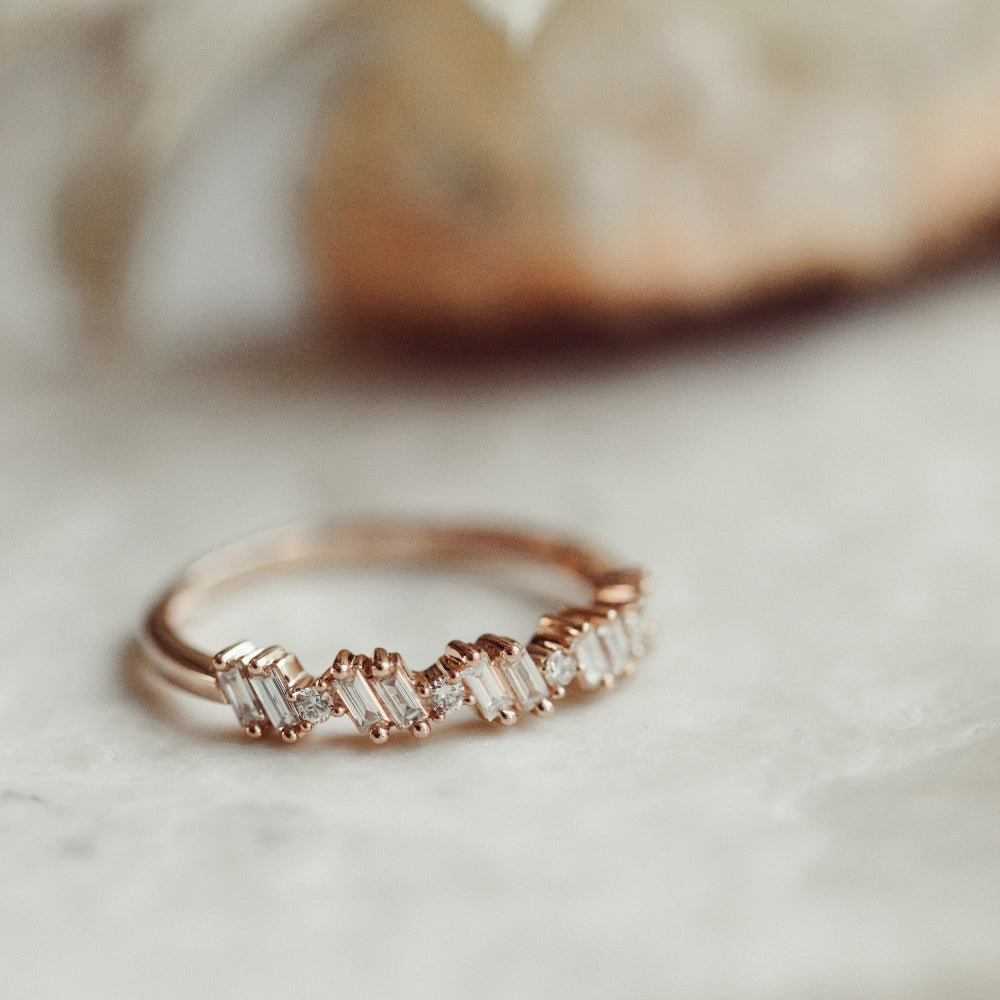 Rose gold ring with diamond wedding band accents on a marble surface.