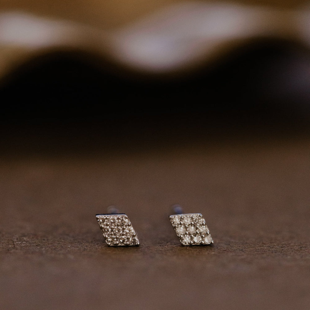Pair of diamond stud earrings on a brown surface.