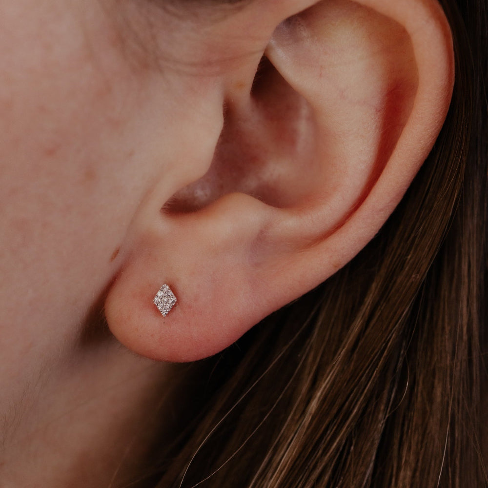 Close-up of an ear wearing a diamond stud earring with brown hair.