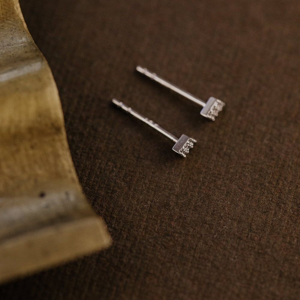 Two gold kite-shaped diamond earrings on a brown fabric background.