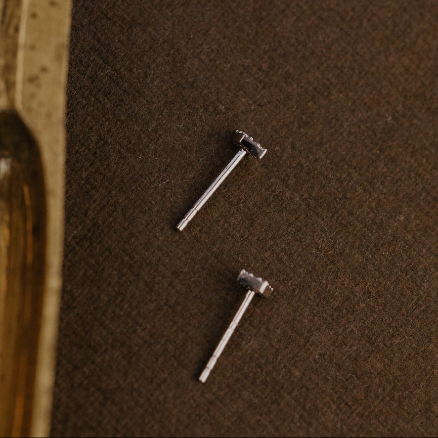 Two gold earrings on a brown textured surface.