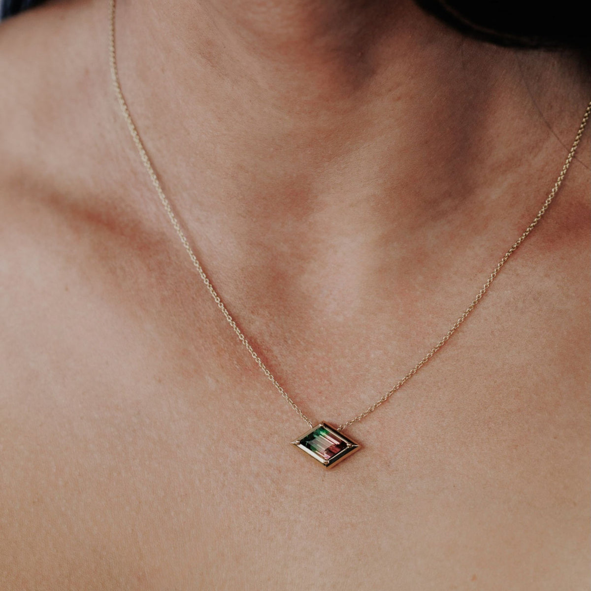 A 14k yellow gold kite shaped tourmaline necklace shown on the neck of a model.