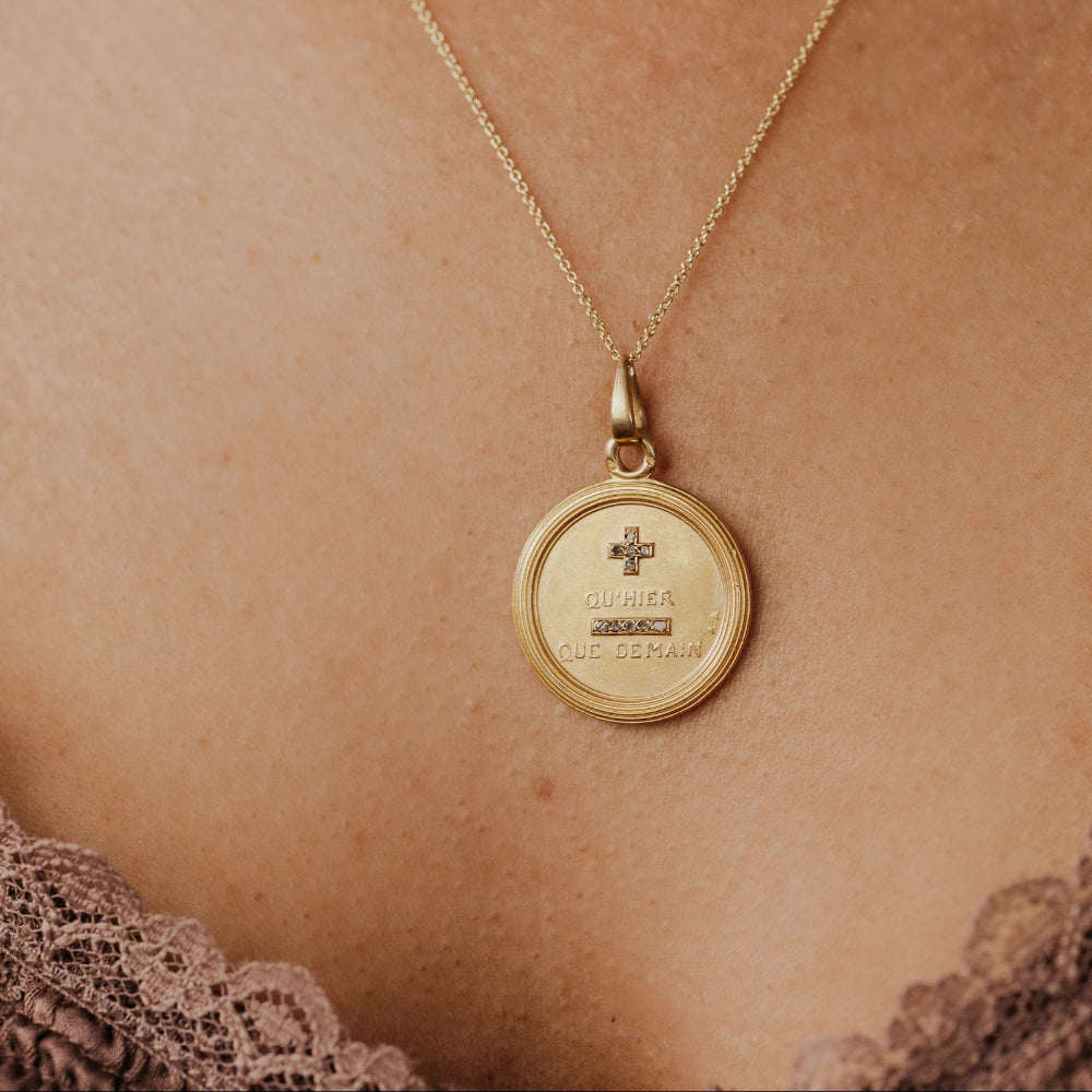 The Large 18k Yellow Gold Vintage Love Token with Diamonds by A. Augis, a round vintage French love token with rose-cut natural diamonds and engraved text, worn on a delicate gold chain against a model's décolletage.