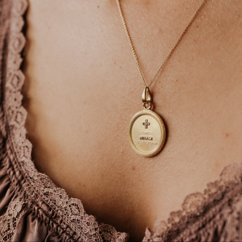 The Large 18k Yellow Gold Vintage Love Token with Diamonds by A. Augis, a round 18k yellow gold pendant with a textured border and rose-cut natural diamonds, shown at an angle on a gold chain against a model's décolletage.
