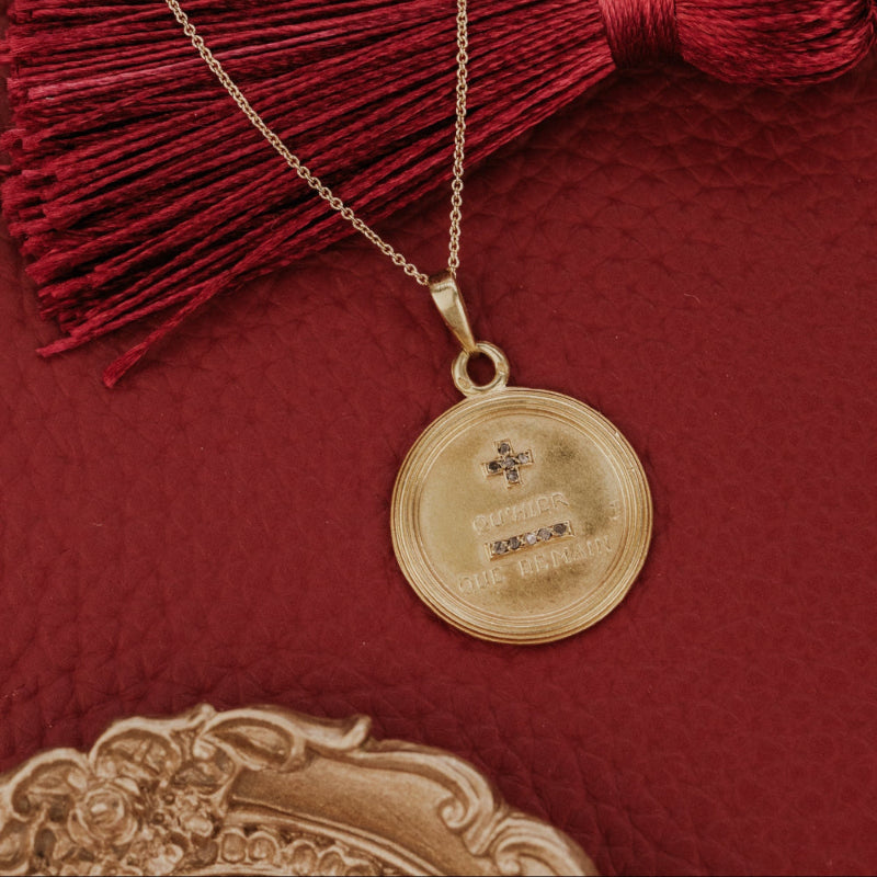 The Large 18k Yellow Gold Vintage Love Token with Diamonds by A. Augis, a round vintage French love token with rose-cut natural diamonds and engraved text, styled on a gold chain alongside a burgundy tassel and ornate props on a deep red surface.