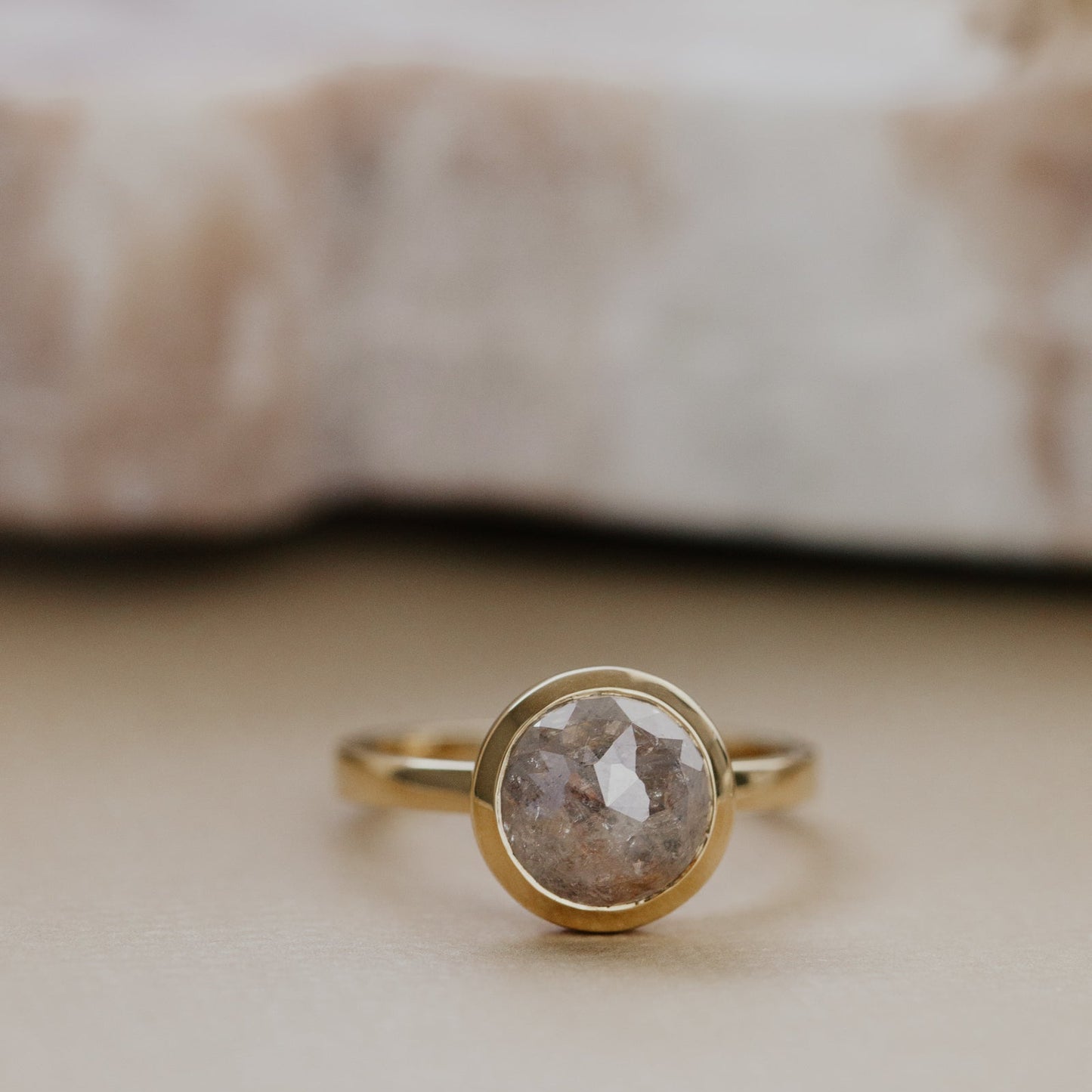 Gold ring with a gray round bezel set rustic diamond on a neutral background.