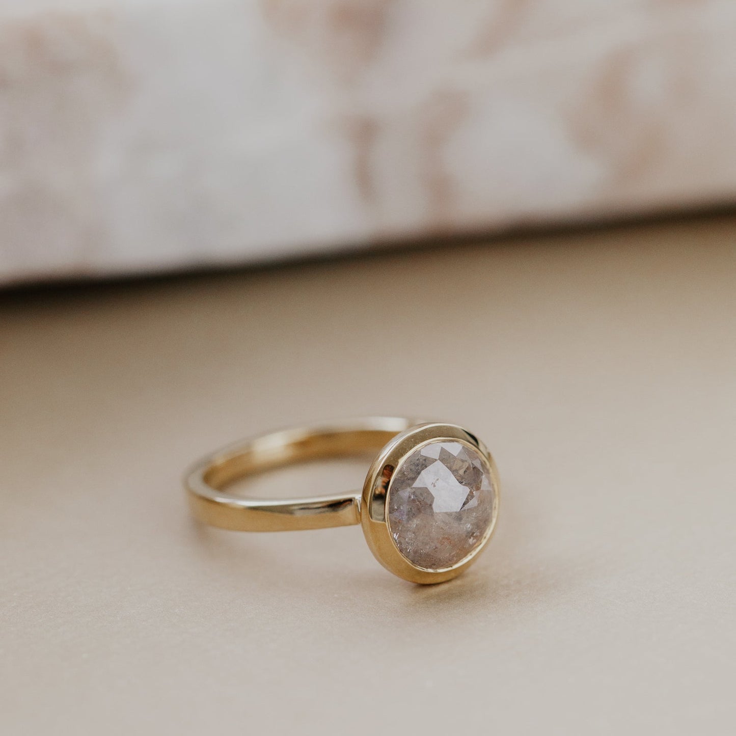 Gold ring with a bezel set round rustic diamond diamond on a marble surface.