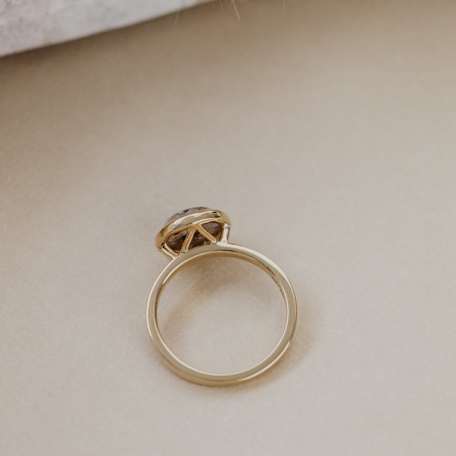 Gold ring with a gray rustic diamond on a beige surface.