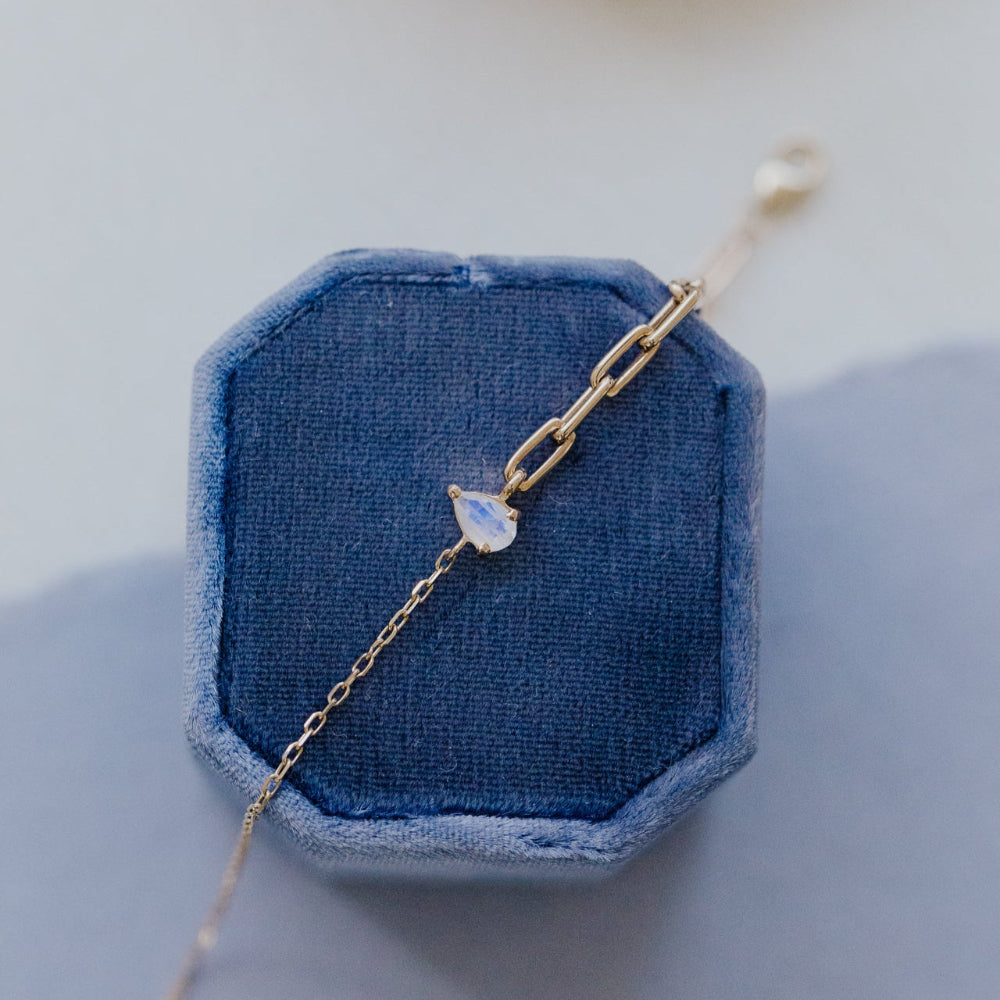 Delicate gold bracelet with a moonstone on a blue jewelry display
