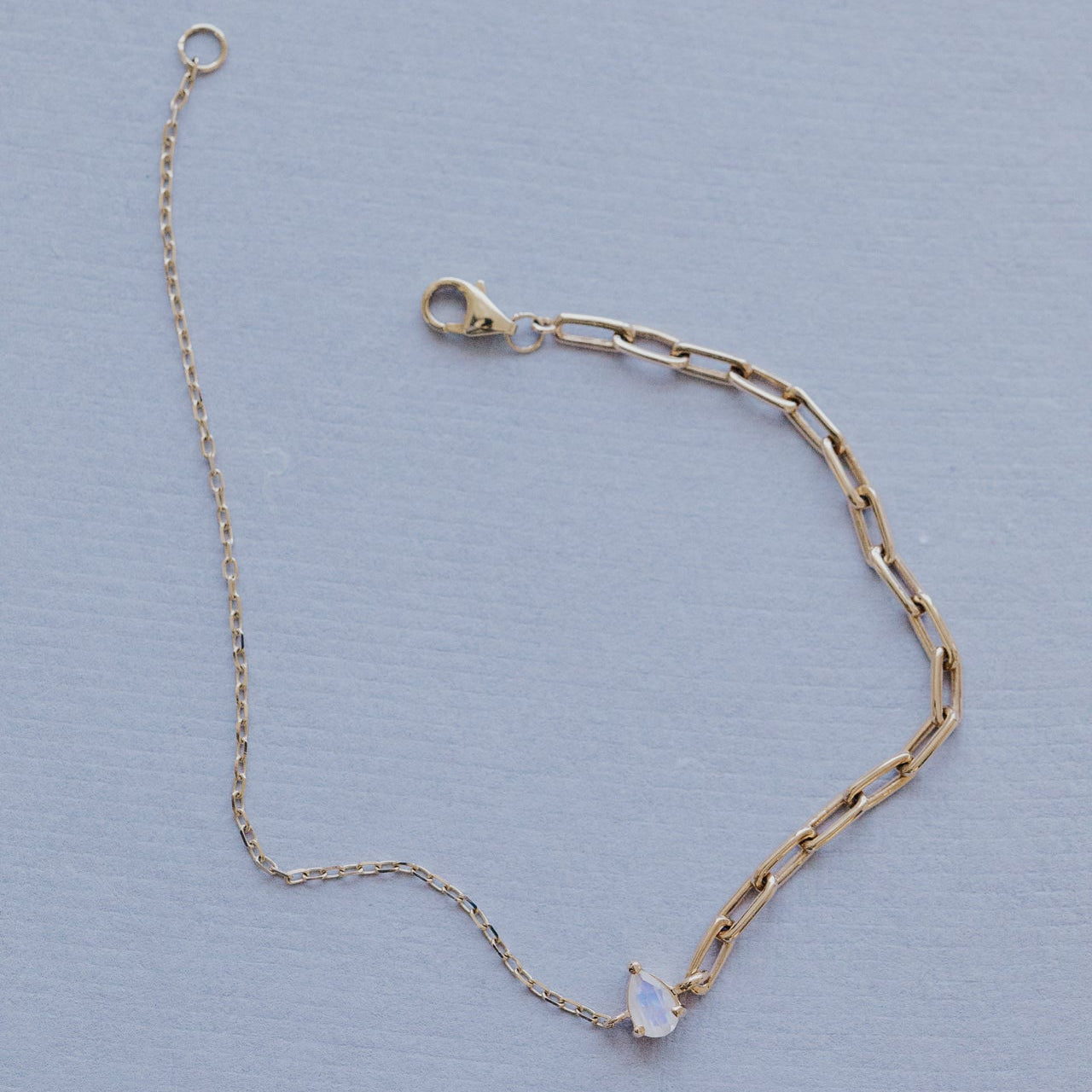 Gold chain bracelet with a moonstone gemstone on a light blue background