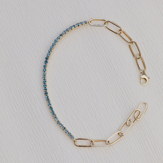 Gold chain bracelet with blue topaz on a light gray background