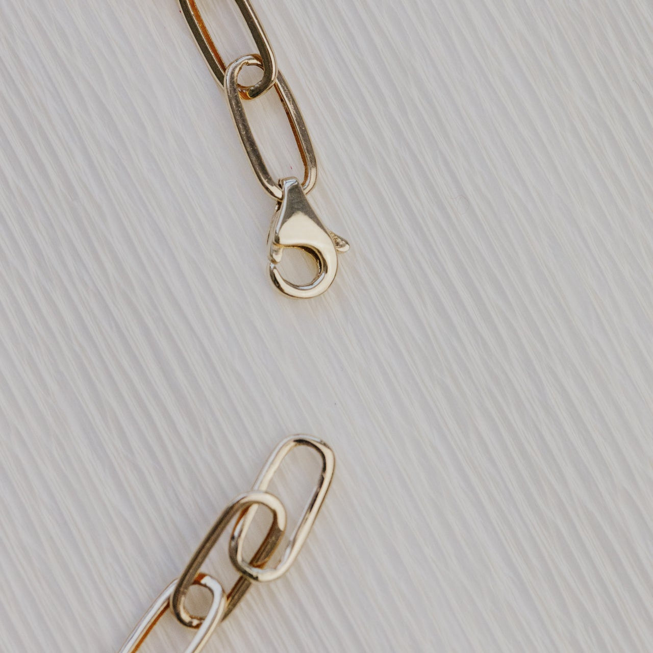 Gold chain bracelet on a textured light gray background