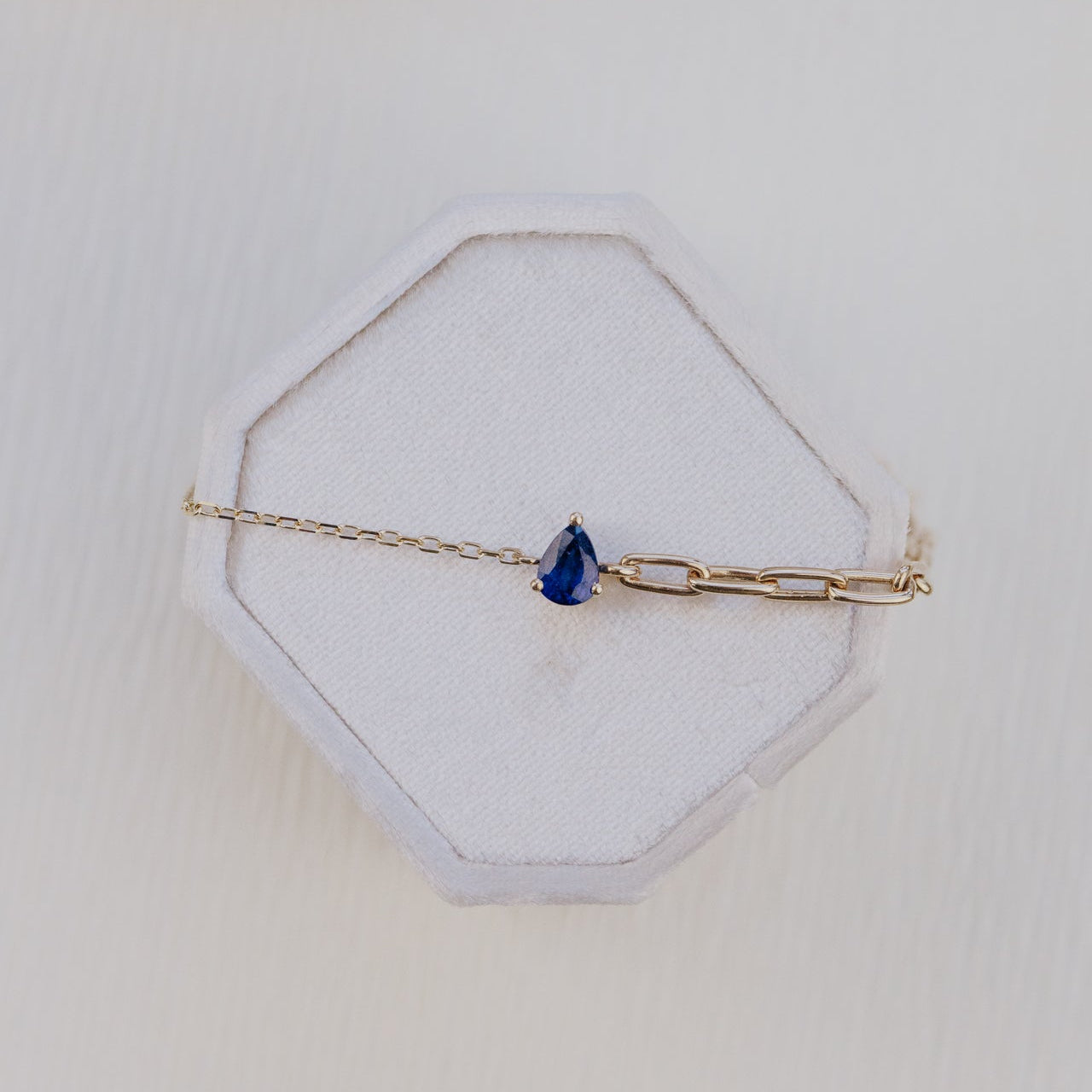 Gold bracelet with a blue sapphire stone on a white hexagonal stand with a shell in the background
