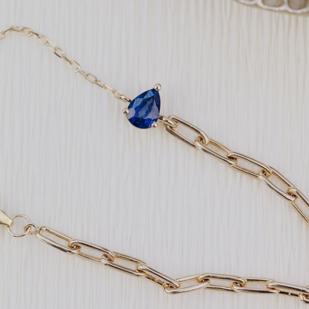 Gold chain bracelet with a blue sapphire gemstone on a textured beige background